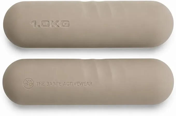 Deux haltères de forme ovale et de couleur beige clair, posées à plat sur un fond blanc. L'haltère supérieure affiche l'inscription "1.0KG" en relief, tandis que l'haltère inférieure porte le logo lotus et le texte "THE BARRE ACTIVEWEAR" en relief.